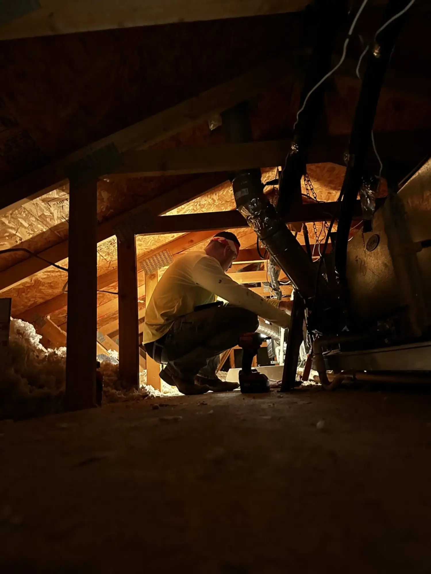 A DC AC Arizona technician kneeling in an attic, working on duct connections at the air handler.