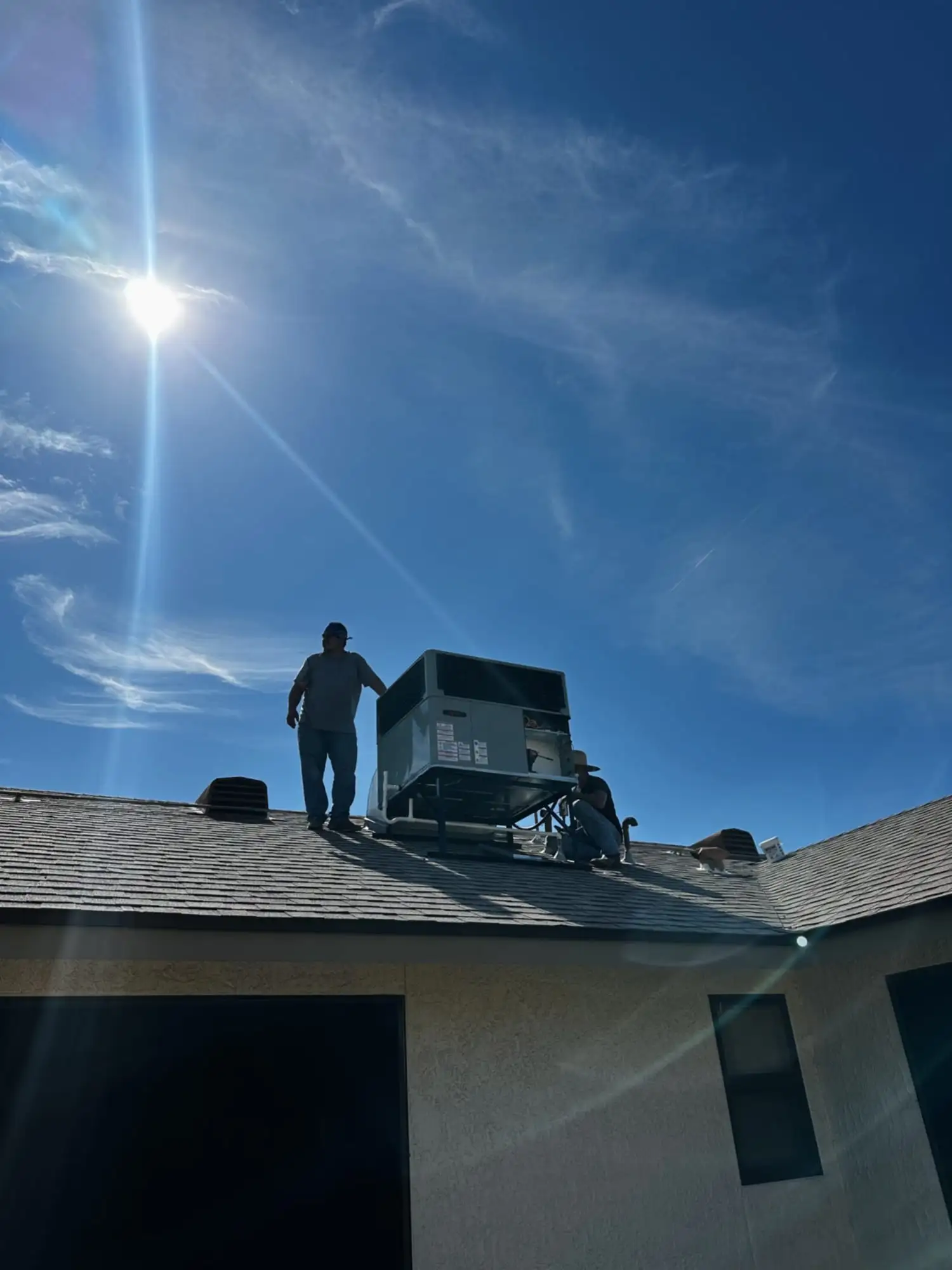 Two DC AC technicians working on a rooftop package unit under a bright desert sun.
